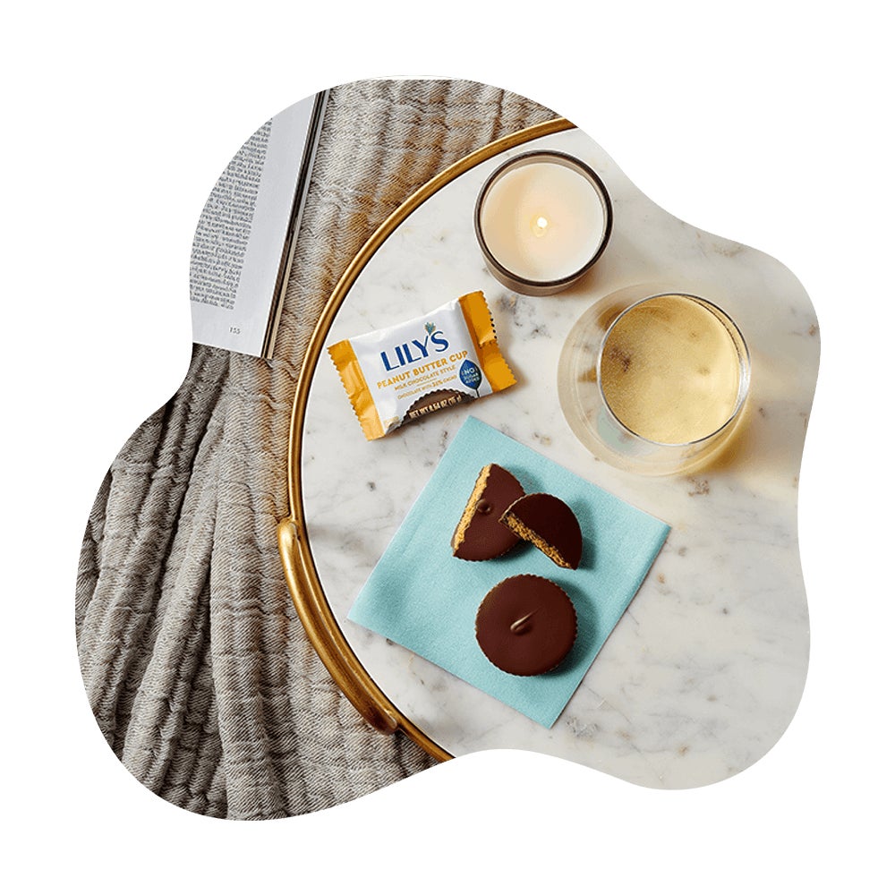 lilys milk chocolate style peanut butter cups on a table beside a book, candle, and beverage